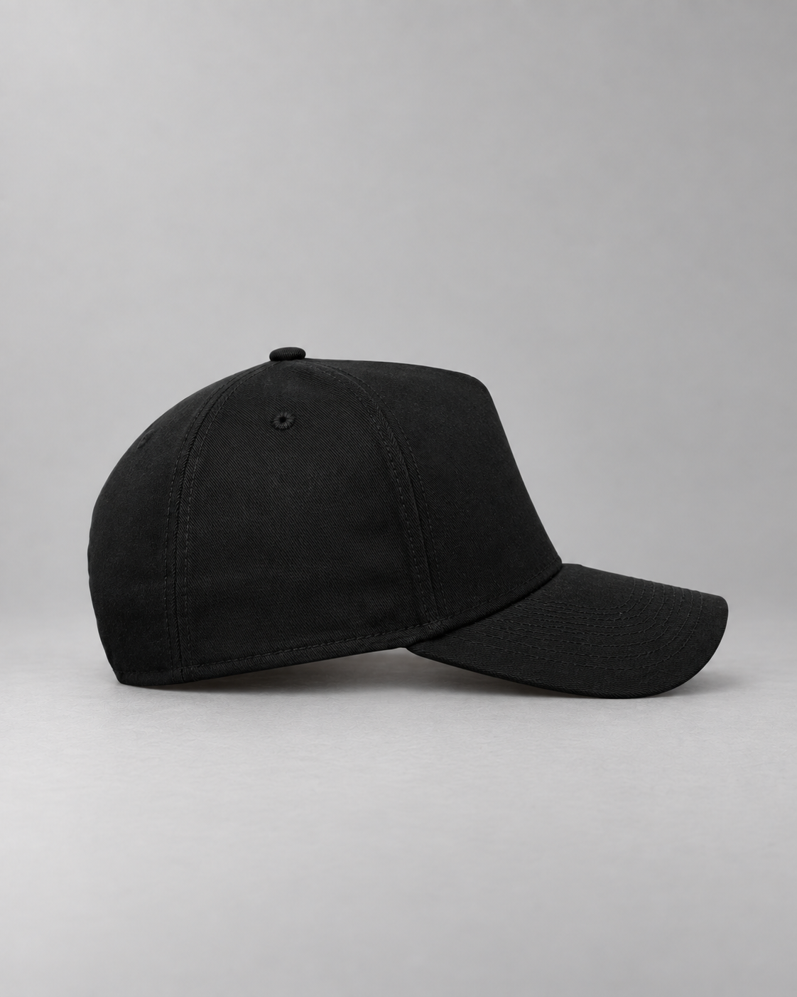 Wearer’s right side of the black cap, showing its curved visor and plain side panel.