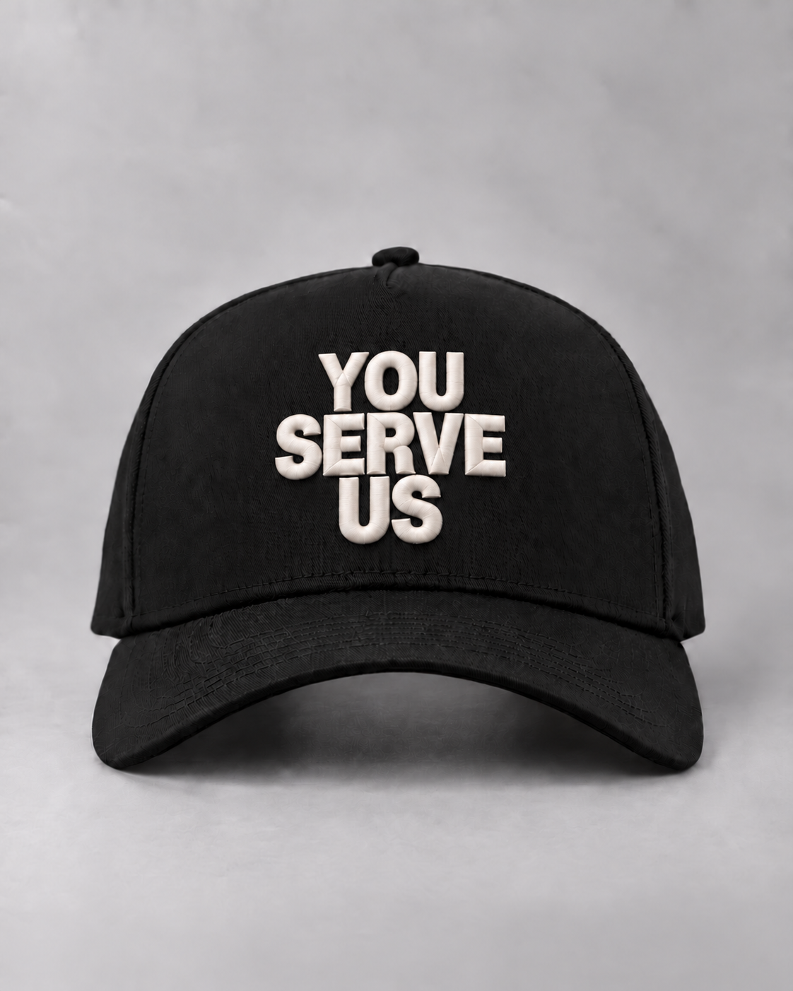 Front view of the black YOU SERVE US cap with raised ivory lettering.